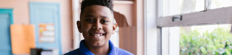 A imagem mostra um menino com um livro aberto em mãos e sorrindo para a foto